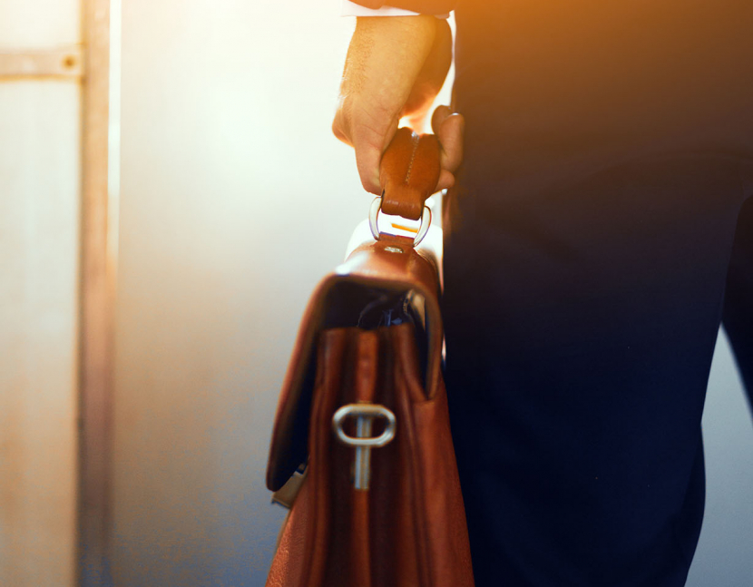Brown leather case in hands of man. Cropped picture of businessman in suit standing in subway train and holding brown bag in his hand.